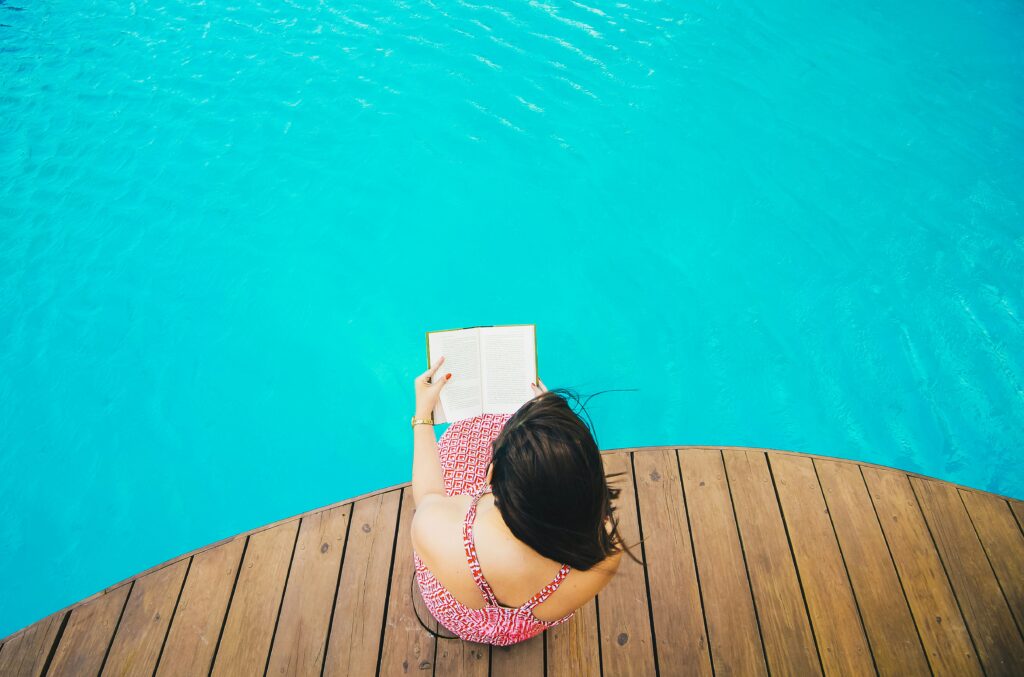 White woman sitting beside a dock reading, hair swinging in the breeze